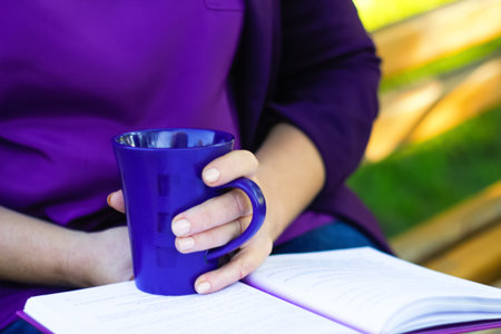 woman reading book mug purple tea outside park nature. a woman or female reading a book outdoors in a park or garden, holding a mug of tea, with a hint of purple color for aesthetic appeal.の写真素材