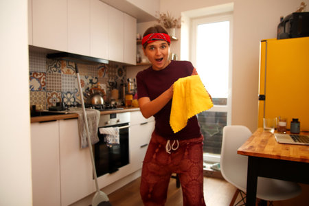 A cheerful woman is captured in a kitchen, demonstrating efficient cleaning with a rag. Her genuine...