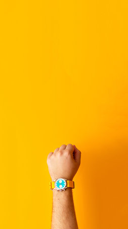 a hand wearing a wristwatch, set against a bright yellow background, to convey the value of time management during the summer or autumn seasons. vertical yellow banner.の写真素材