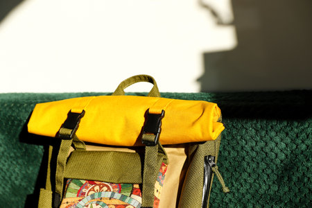 Stylish rolled-top yellow and green backpack with colorful patterned pocket on emerald velvet surface, sunlight. Tapestry and waterproof fabric.の写真素材