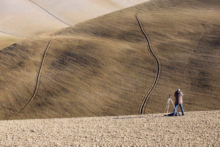 Photographer on plough Tuscany field with Furrows in curved Linesの写真素材