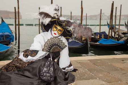 Portrait of Female Venetian Mask in black and white elegant costume with venetian gondolas, St. Mark's Square, Venice, Italyのeditorial素材