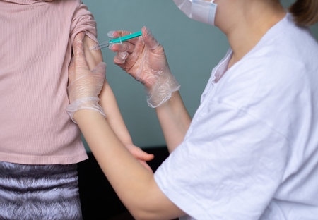 Little child vaccinated by doctor in medical mask. Nurse giving an injection to a patient, close-up.