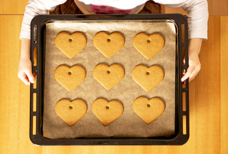Many homemade fresh baked heart cookies on a baking sheet in the hands of a girl. Valentine's Day...
