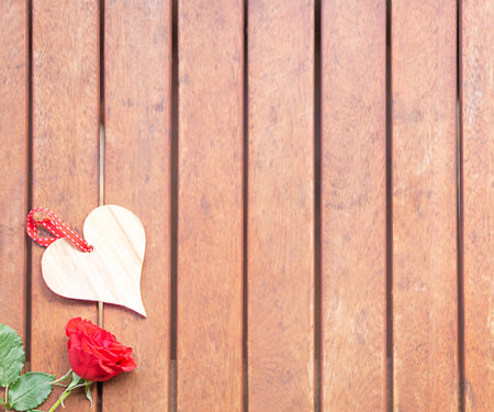 Bright wooden heart and red rose below left on the brown vintage wooden background.の写真素材