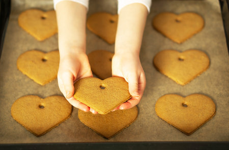 Girl hands holding a heart cookie in front of the homemade fresh baked cookies on baking sheet.