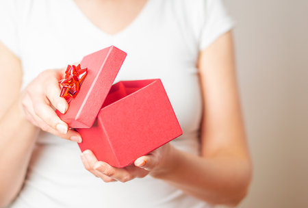 Female hands opening a small gift in a red box with a heart.の写真素材