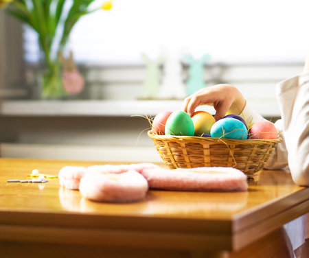 Little child, five years old, playing with colored Easter eggs in a basket on wooden table