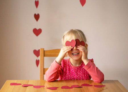 A girl crafting hearts from red paper. Background for valentines day or mothers day.の写真素材