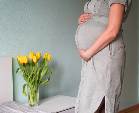 Pregnant woman in dress standing and holding hands on big belly. Pregnancy and motherhood concept.の写真素材
