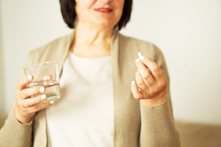 Retired woman in casual clothes at home holding pill and glass water.の写真素材