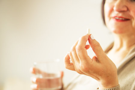 Close up of a retired woman in casual clothes at home holding pill and glass water.の写真素材