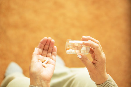 Close up of old female hands holding pills and puoring capsules from the bottle.の写真素材