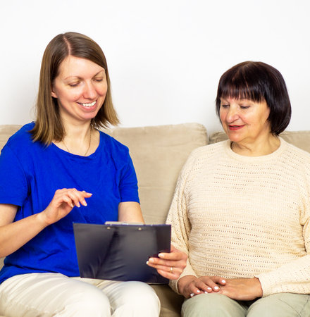 Young caregiver showing a precsription or document and helping senior woman at home.の写真素材