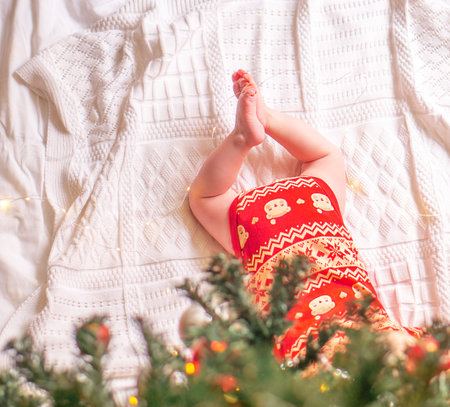 Small baby legs on the blanket under green decorated christmas tree.の写真素材
