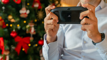 Istanbul, Turkey - November 2019: Man playing with Sony PS Vita with a christmas tree at the back