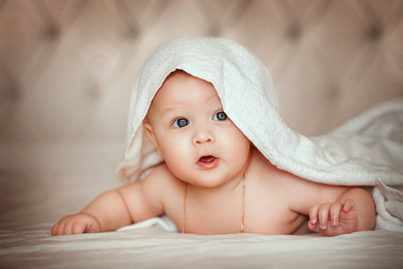 6 month old baby on the bed covered with a white towel