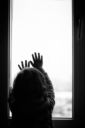 little boy looking out the window holding his hand over the glass black whiteの写真素材