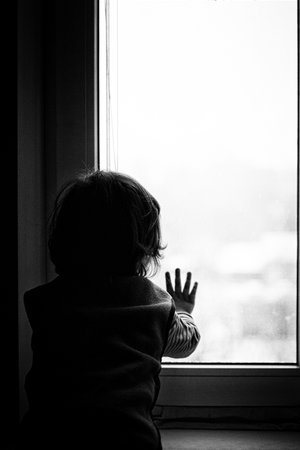 little boy looking out the window holding his hand over the glass black whiteの写真素材