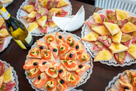 a lot of different sandwiches with salmon caviar cheese sausage on the table with a bottle of wine