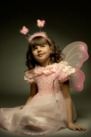 beautiful  little girl with wings, sit and  smile on dark backgroundの写真素材