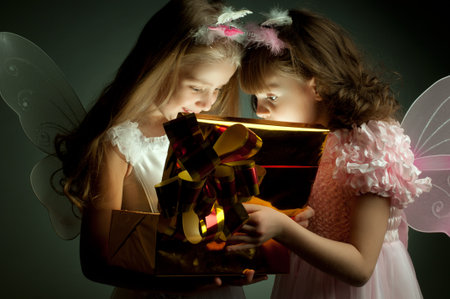 two little girl examine gift in fancy box, smile, on dark backgroundの写真素材