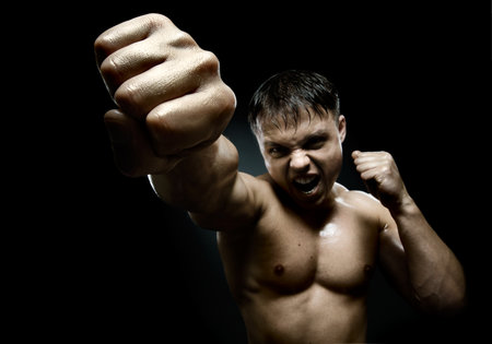 horizontal photo  muscular young  guy street-fighter, cuff  fist close up on camera and yell , hard lightの写真素材