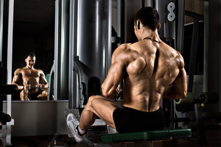 very power athletic guy bodybuilder,  execute exercise with gym apparatus, on broadest muscle of backの写真素材