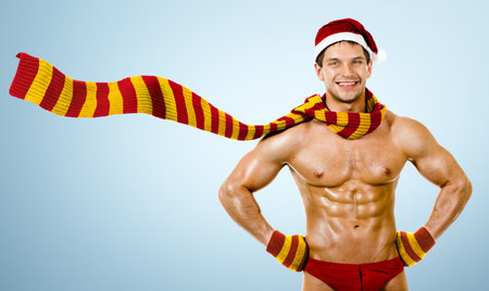 the very muscular  bronzed handsome sexy Santa Claus in striped red-yellow  muffler, smile, on light blue backgroundの写真素材