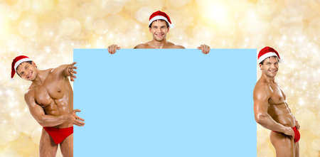 three muscular  bronzed handsome sexy Santa Claus, look out from board and smileの写真素材