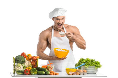 Man bodybuilder in white toque blanche and cook protective apron, eating cottage cheese , on whie background, isolatedの写真素材