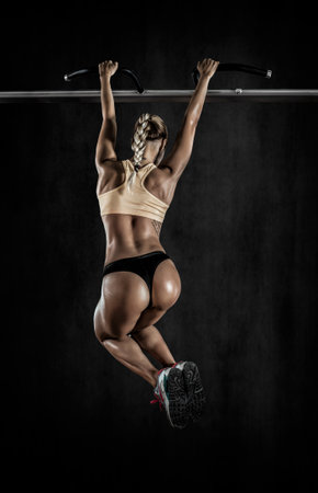 young fitness woman chin-up on horizontal bar on black background with empty space for text,...
