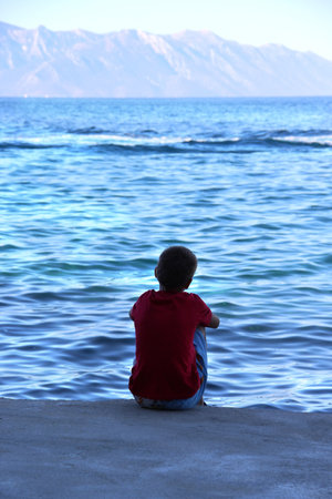 Small boy sitting on the coast of Adriatic sea and looking at water の写真素材