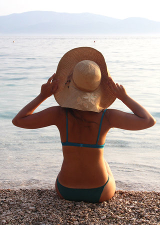 Young beautiful woman in straw hat sitting on the beach 
