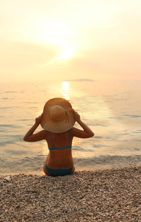 Young beautiful woman in straw hat sitting on the beach の写真素材