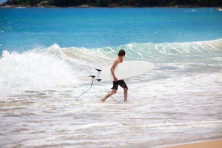 A young man finished surf in the ocean, walking up with surf boad in handsの写真素材