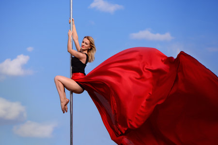 Sportish smiling girl makes acrobatic element at pole dance