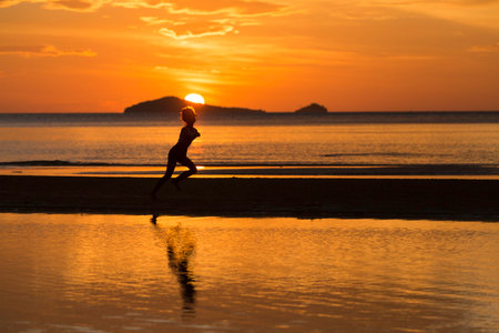 the silhouette photo of asian girl enjoy running on the beach with colorful sea in sunriseの写真素材