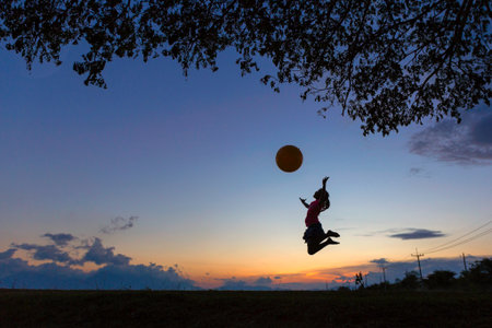 A schoolgirl juming with big ball under the tree in sunset.の写真素材
