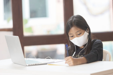 An Asian schoolgirl wears a mask and is studying online at home during the corona virus epidemic.の写真素材