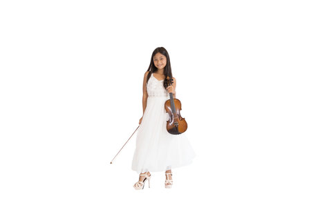 A portrait of a cute, elementary school Asian girl with long hair and wearing a white evening dress holding her violin. An isolated image with white backgroundの写真素材