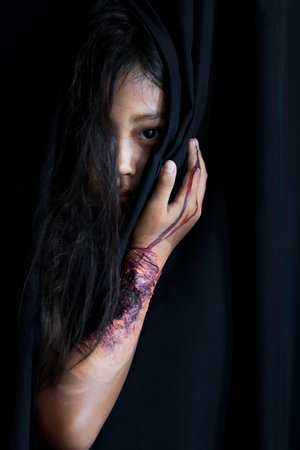 An Asian girl makes up her hair and creates an artificial wound with blood marks on her arm to...