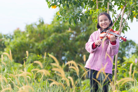 A portrait of an Asian girl and her violin in the morning meadow during a holiday on the mountainの写真素材