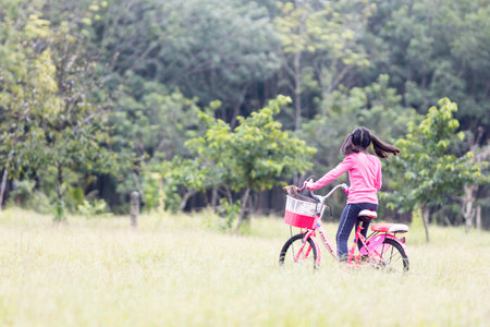 A cute Asian schoolgirl with long hair enjoying a bike ride with her puppy.の写真素材