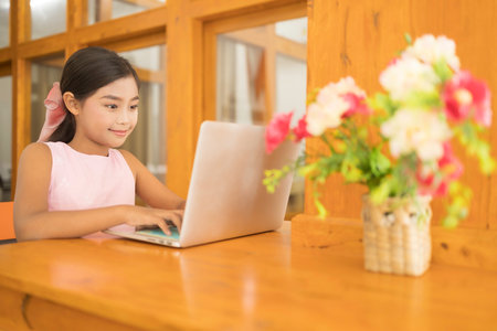 A cute Asian schoolgirl is using a laptop to study online in the living room at home while the corona virus is spreading. Concept of Coronavirus quarantine.の写真素材