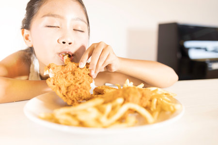 A cute Asian girl is enjoying eating fried chicken and French fries.の写真素材
