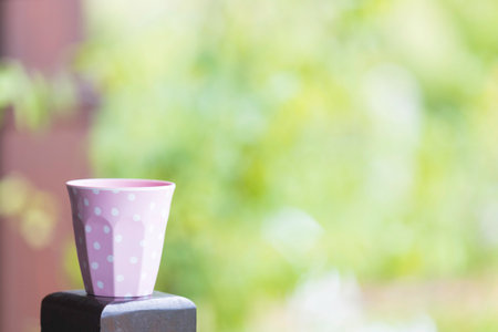 A pink ceramic mug with white spots resting on a wooden pole in the garden.の写真素材