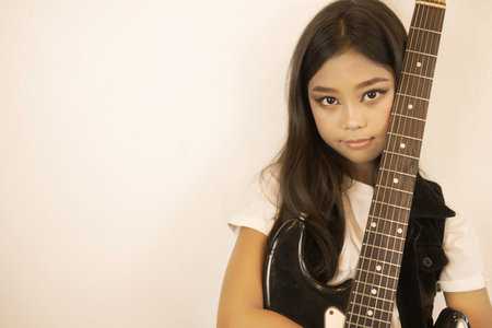 A portrait of a cute Asian girl in a make-up standing to hug her electric guitar.