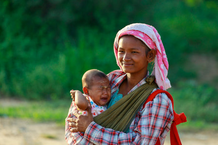 Bagan/Myanmar-October4th 2019: A native Burmese woman is carrying a baby asking for money from a tourist who visits an ancient pagoda in Bagan, Myanmar.のeditorial素材