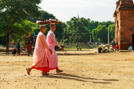 Bagan/Myanmar-October 4th 2019: Two Burmese middle-aged nuns put a basket on their heads to make merit at the temple.のeditorial素材